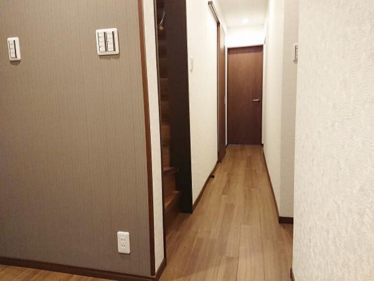 【リフォーム済】1階廊下写真。天井・壁はクロス貼替え、床はウッドタイルで仕上げました。照明器具も全て新品に交換し、広く明るい廊下に生まれ変わりました。