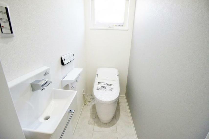 タンクレストイレ・サイドの手洗い器・さりげないグレーのアクセントクロスがお洒落なトイレ