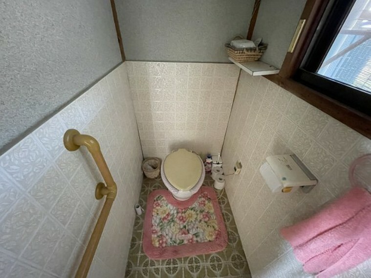トイレ 白色の清潔感のあるトイレです。手すりもあり、バリアフリーな作りですね。窓もあるので換気もきちんとできます。ちょっとした物を置いておくのに、上部の棚が便利です。