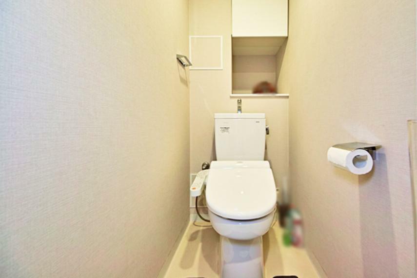 白を基調としたシンプルで清潔感あるトイレ。トイレットペーパーの予備や掃除用具も収納できる棚も完備