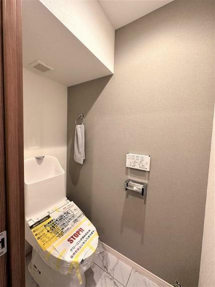 トイレ グレーのアクセントクロスで落ち着きのある空間を演出！スペースが広いので角に棚を置いても圧迫感なし